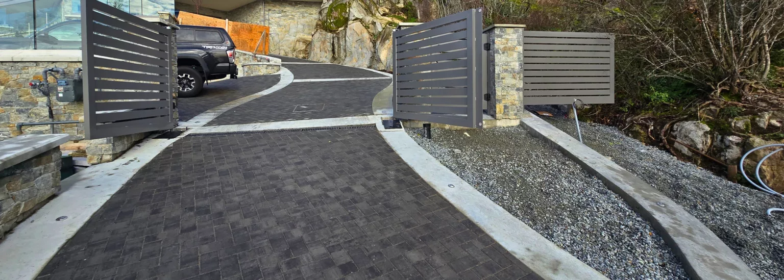 Modern gated driveway with dark pavers and concrete edging at luxury home in West Vancouver